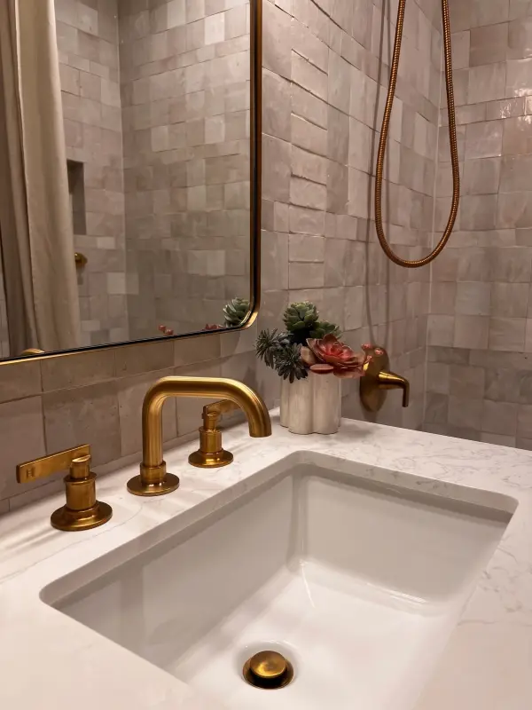 Brushed brass faucet on a quartz vanity against handmade glazed tile