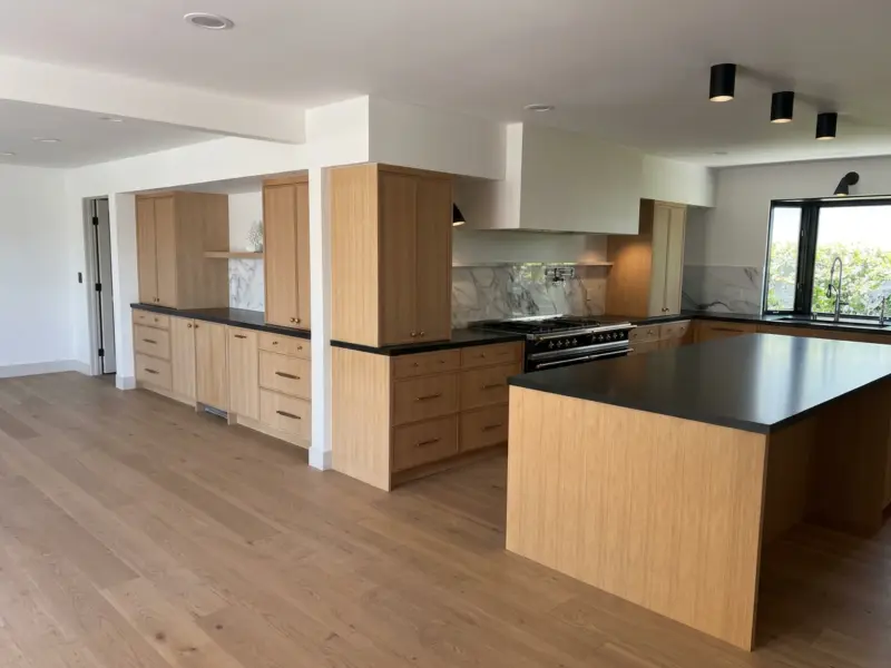 Open-plan white oak kitchen with a black quartz island and wide-plank oak floor